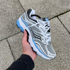Saucony ProGrid Omni 9 Blissful Blue – white, silver and baby blue retro running trainer held in hand, front lateral top-down view showing mesh upper and white laces against paving stones