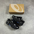 ASICS Gel Venture 6 Blue Coast – pair of black chunky trail trainers with white ASICS Stripes and blue GEL accents, flat lay top-down view alongside ASICS branded shoebox on concrete surface