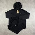 Nike Repel Tracksuit Black – black jacket with white Nike Swoosh and reflective detailing, paired with matching black joggers with Swoosh logo, flat lay on concrete surface with tags attached