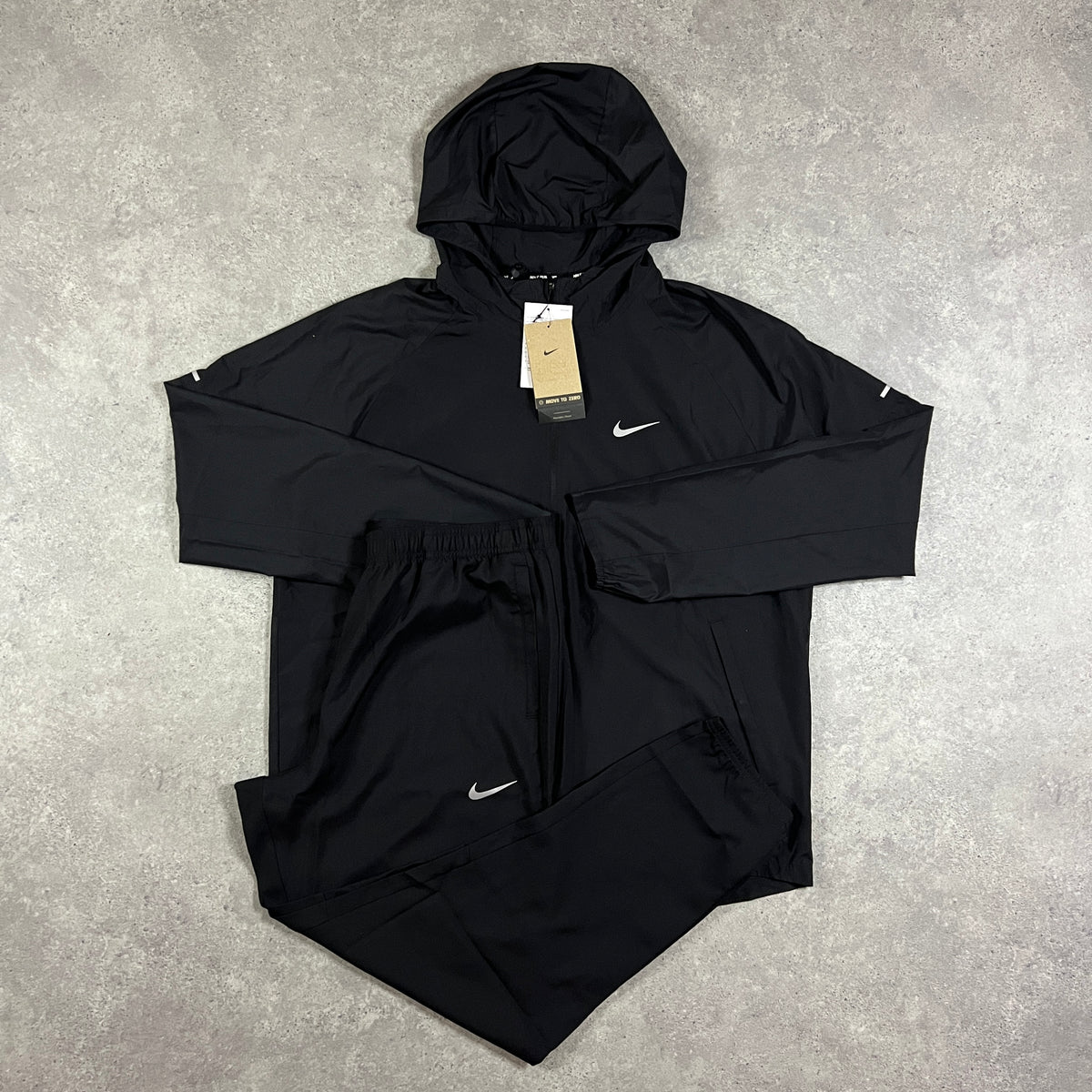 Nike Repel Tracksuit Black – black jacket with white Nike Swoosh and reflective detailing, paired with matching black joggers with Swoosh logo, flat lay on concrete surface with tags attached